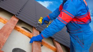 A worker places metal roof tiles on a roof.