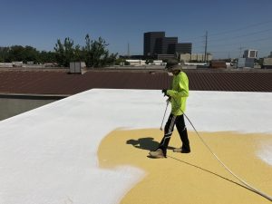 A worker sprays roof coatings