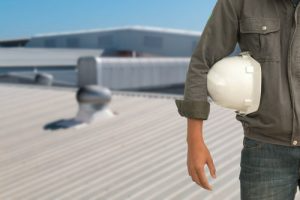 A man holds a hard hat as he stands on a roof